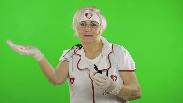 Elderly caucasian female doctor nurse points at something with her hands — Stock fotografie