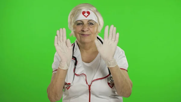 Elderly caucasian female doctor in protective mask. Waving her hands — Stockfoto