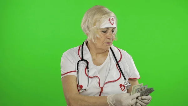 Elderly caucasian female doctor receives money. Counts money — Stok fotoğraf