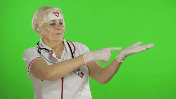 Elderly caucasian female doctor nurse points at something with her hands — Stockfoto