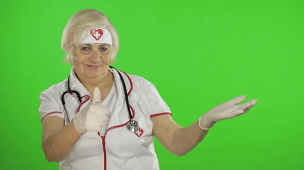 Elderly caucasian female doctor nurse points at something with her hands — Stockfoto