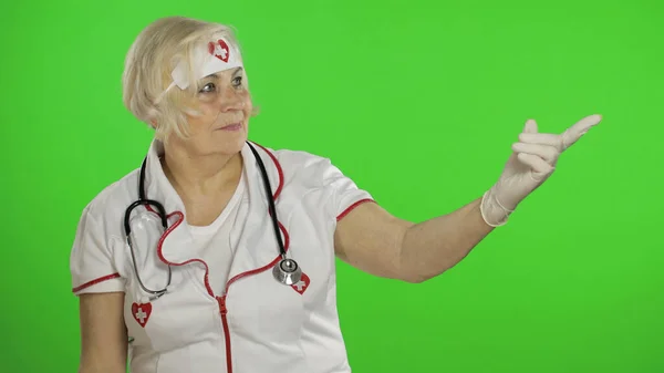 Elderly caucasian female doctor nurse points at something with her hands — Φωτογραφία Αρχείου