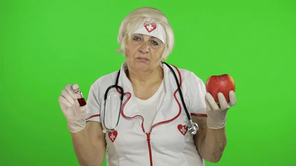 Portrait of elderly caucasian female doctor chooses treats medications or fruits — Stockfoto