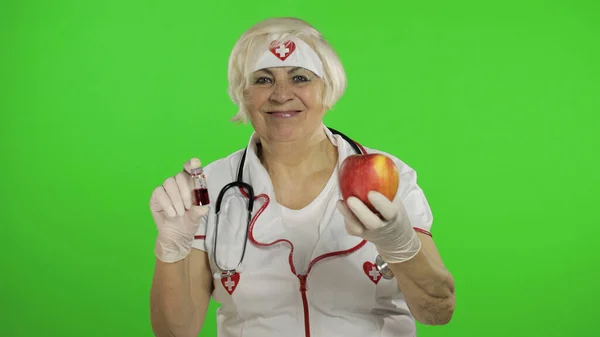 Portrait of elderly caucasian female doctor chooses treats medications or fruits — Stockfoto