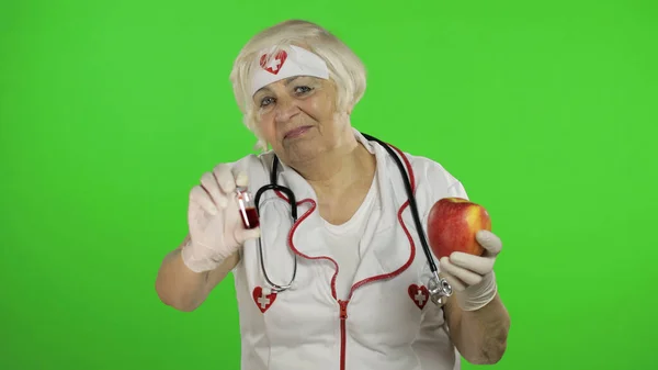 Portrait of elderly caucasian female doctor chooses treats medications or fruits — Stock fotografie