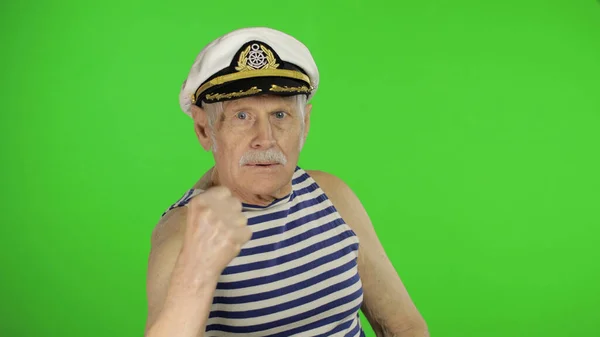 Elderly sailor man is angry and shows a fist. Sailorman on chroma key background