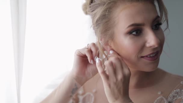 Vacker och härlig brud i brudklänning och slöja sätter på örhängen — Stockvideo