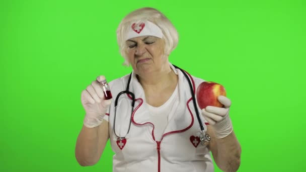 Portrait of elderly caucasian female doctor chooses treats medications or fruits — Stock Video