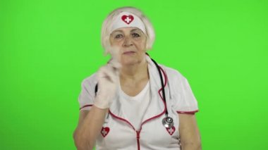 Elderly caucasian female doctor in protective mask. Waving her hands. Warning