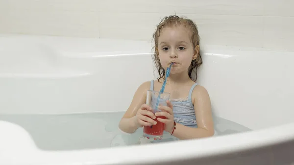 Schattig blond meisje neemt een bad in badmode en drinkt een cocktail. Klein kind — Stockfoto