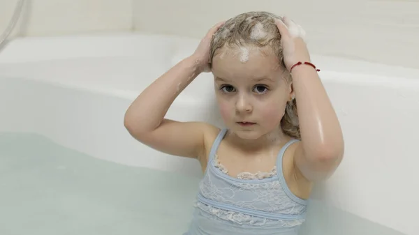 Nettes blondes Mädchen nimmt ein Bad in Badebekleidung. Kleines Kind wäscht sich den Kopf — Stockfoto