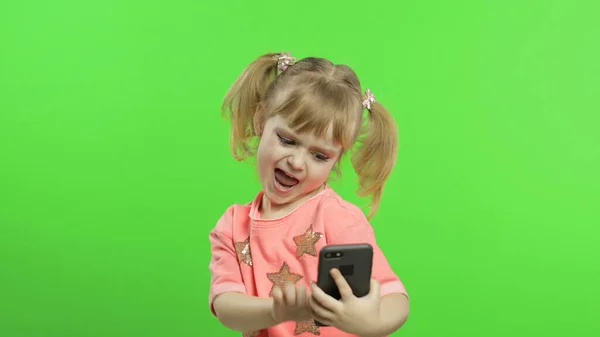 Egy kislány okostelefont használ. Portré gyermek okostelefon szöveges, játék — Stock Fotó