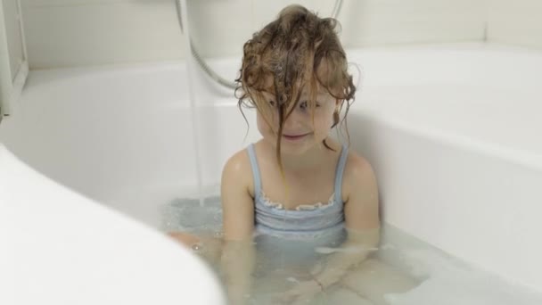 Nettes blondes Mädchen nimmt ein Bad in Badebekleidung. Kleines Kind wäscht sich den Kopf — Stockvideo