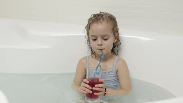 Menina loira bonito toma um banho em roupa de banho e beber um cocktail. Criança — Vídeo de Stock