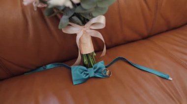 Güzel düğün buketleri, alyansları ve damat papyonlarıyla kanepede yatar.