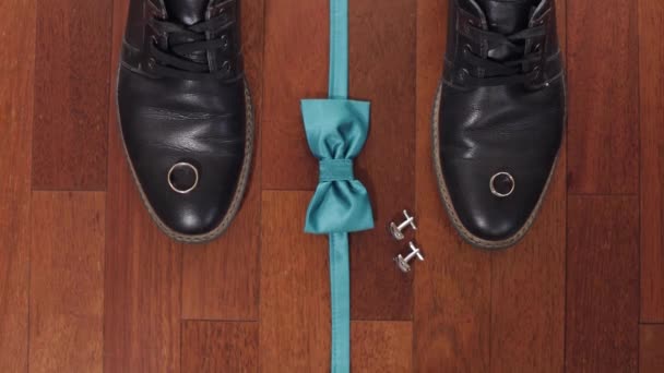 Anneaux de mariage, noeud papillon vert marié, boutons de manchette et chaussures sur plancher de bois brun — Video