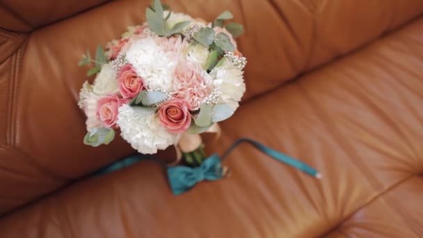 Gyönyörű esküvői csokrok feküdnek jegygyűrűvel és vőlegény csokornyakkendő kanapén — Stock videók