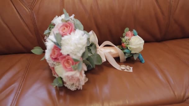 Gyönyörű esküvői virág csokrok feküdnek jegygyűrűvel a barna kanapén. — Stock videók