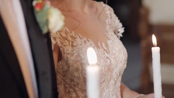 Νιόπαντροι. Η νύφη και ο γαμπρός στέκονται στην εκκλησία κρατώντας κεριά στα χέρια τους. — Αρχείο Βίντεο