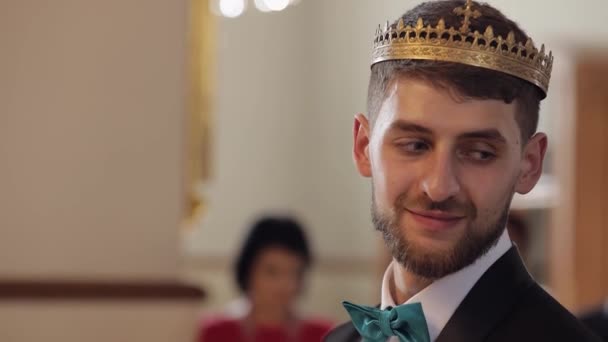 Наречений у короні стоїть у церкві. Він дивиться на наречену і посміхається. молодята — стокове відео