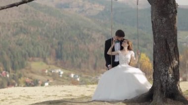 Yeni evliler. Beyaz damat ve gelin bir dağ yamacında salıncakta sallanıyor.