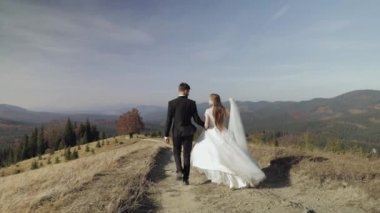 Yeni evliler. Dağın yamacında yürüyen beyaz bir damat ve gelin. Düğün çifti