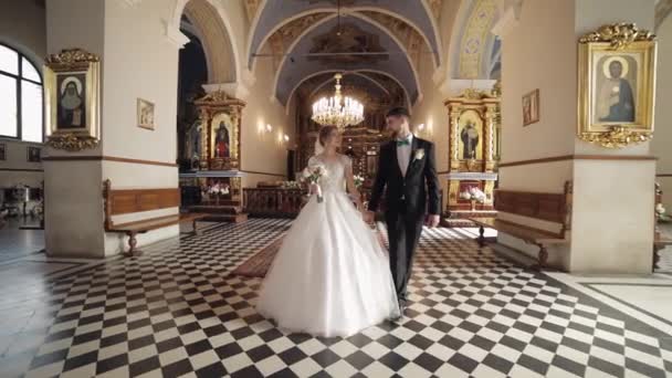 Sposi novelli. Sposi caucasici che camminano insieme in una vecchia chiesa. Matrimonio — Video Stock