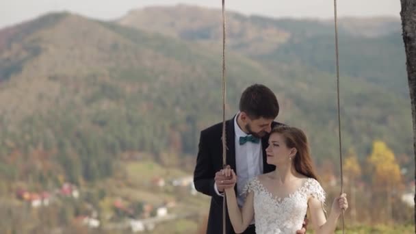 Frisch verheiratet. Kaukasischer Bräutigam mit Braut auf einer Seilschaukel am Berghang — Stockvideo