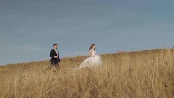 Recién casados. novio caucásico con novia corriendo en la ladera de la montaña. Pareja de boda — Vídeo de stock