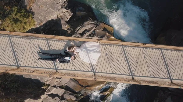 Novomanželé. Nevěsta a ženich leží na mostě přes horskou řeku. Letecký pohled — Stock fotografie