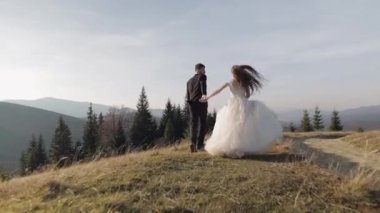 Yeni evliler. Dağın yamacında koşan beyaz bir damat ve gelin. Düğün çifti