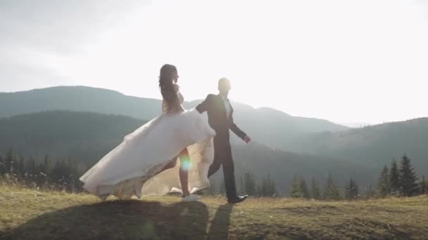 Les jeunes mariés. marié caucasien avec mariée courant sur la pente de la montagne. Couple de mariage — Video