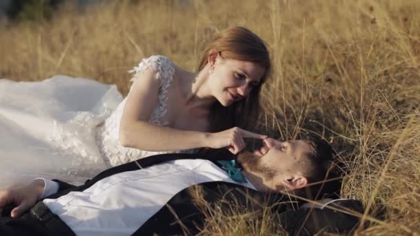 Newlyweds. Caucasian groom with bride lie on the grass on mountain slope — Stock Video