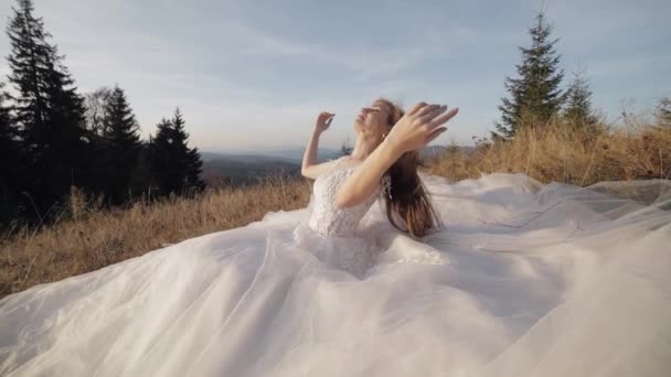 Vacker och härlig brud i bröllopsklänning sitter på gräs på bergssluttningen — Stockvideo