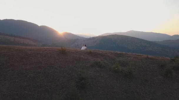 Recién casados corriendo en una ladera alta de la montaña. Novio y novia. Vista aérea — Vídeo de stock