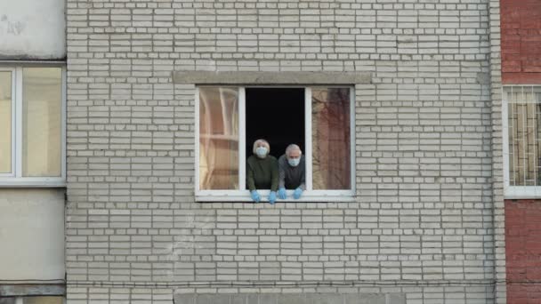 Los abuelos viejos se quedan en la ventana aislados en casa en cuarentena. Coronavirus — Vídeos de Stock