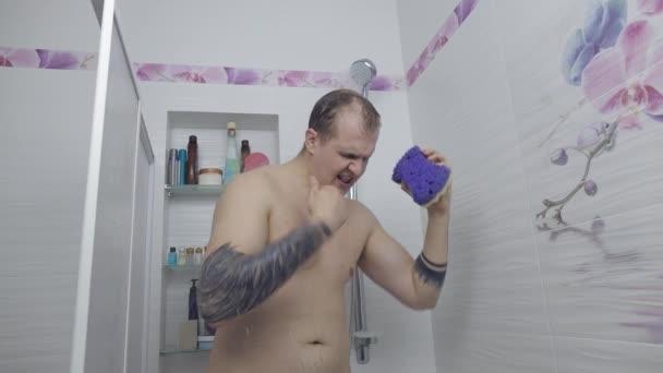 Joven hombre gordo guapo toma una ducha en el baño. Emocionalmente canta y baila — Vídeos de Stock