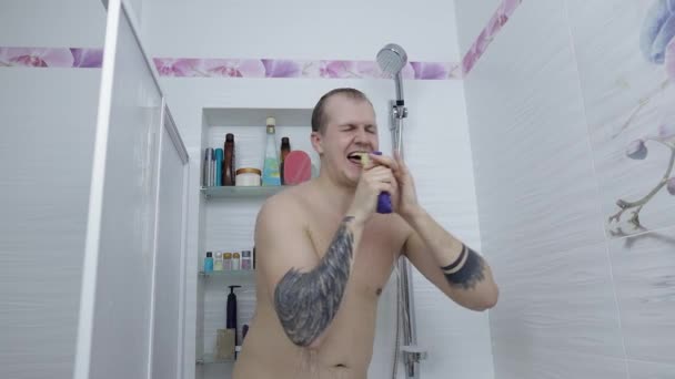 Joven hombre gordo guapo toma una ducha en el baño. Emocionalmente canta y baila — Vídeo de stock