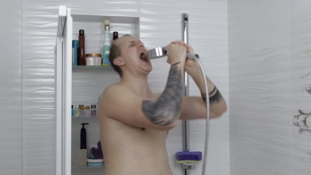 Joven hombre gordo guapo toma una ducha en el baño. Emocionalmente canta y baila — Vídeos de Stock