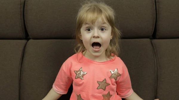 Pozytywna dziewczyna emocjonalnie zrobić twarze i uśmiech w różowej bluzce na kanapie w domu — Zdjęcie stockowe