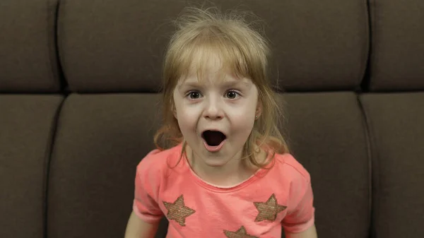 Positiv flicka känslomässigt göra ansikten och le i rosa blus på soffan hemma — Stockfoto