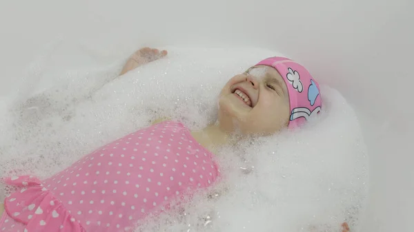 Χαριτωμένο ξανθό κορίτσι κάνει μπάνιο με μαγιό. Μικρό παιδί ξαπλωμένο στο μπάνιο — Φωτογραφία Αρχείου