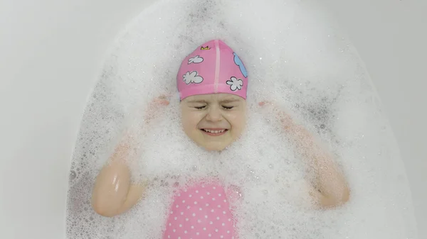 Nettes blondes Mädchen nimmt ein Bad in Badebekleidung. Kleines Kind liegt in der Badewanne — Stockfoto