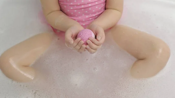 Mädchenhände setzen Badebombe ins Wasser. Badesalzkugel löst sich in Wasser auf — Stockfoto