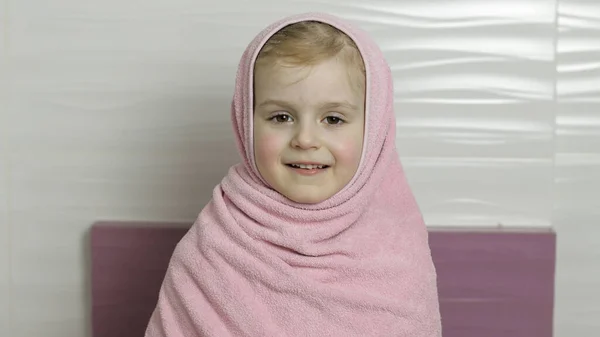 Holčička s mokrými vlasy se schovává v růžovém ručníku. Úsměv po koupeli — Stock fotografie