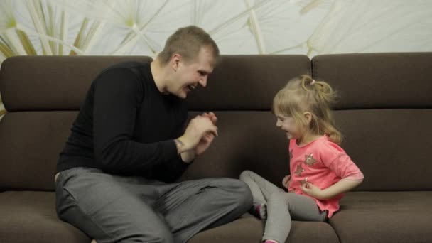 Отец и маленькая дочь смеются, играют вместе на диване. Досуг — стоковое видео