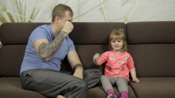 Батько і маленька донька грають ножиці на дивані на рок-папері. Дозвілля гра — стокове відео