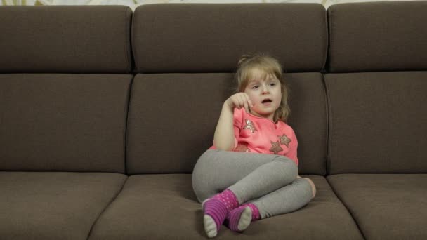 Menina positiva emocionalmente fazer rostos e sorrir em blusa rosa no sofá em casa — Vídeo de Stock