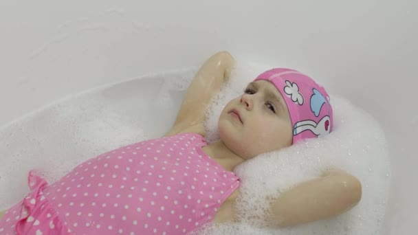 Cute blonde girl takes a bath in swimwear. Little child washes her head — Stock Video