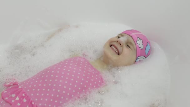 Cute blonde girl takes a bath in swimwear. Little child washes her head — Stock Video